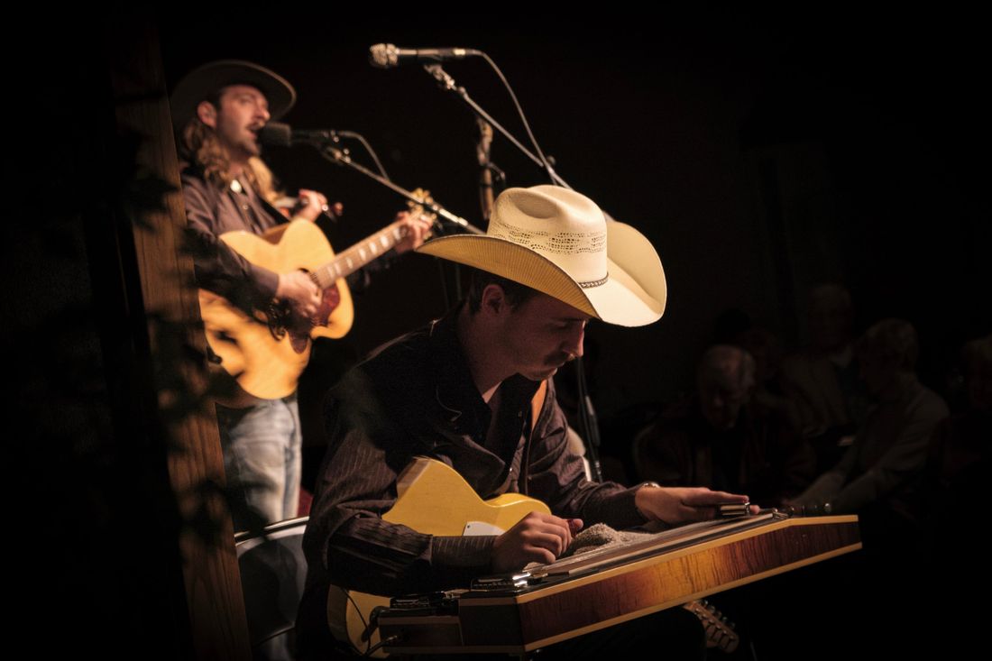 Steel guitar player in a straw cowboy hat with the singer behind him